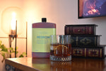 A bottle of Letterbox Cocktails Negroni cocktail mix stands on a wooden table next to a glass of the mixed drink, with decorative books and a warm lamp in the background.