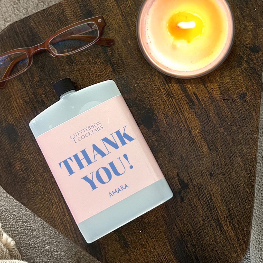 Bottle of 'Thank You!' amara with a candle and glasses on a wooden surface