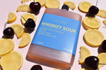 Bottle of whiskey sour mix with lemons and cherries on a light pink background